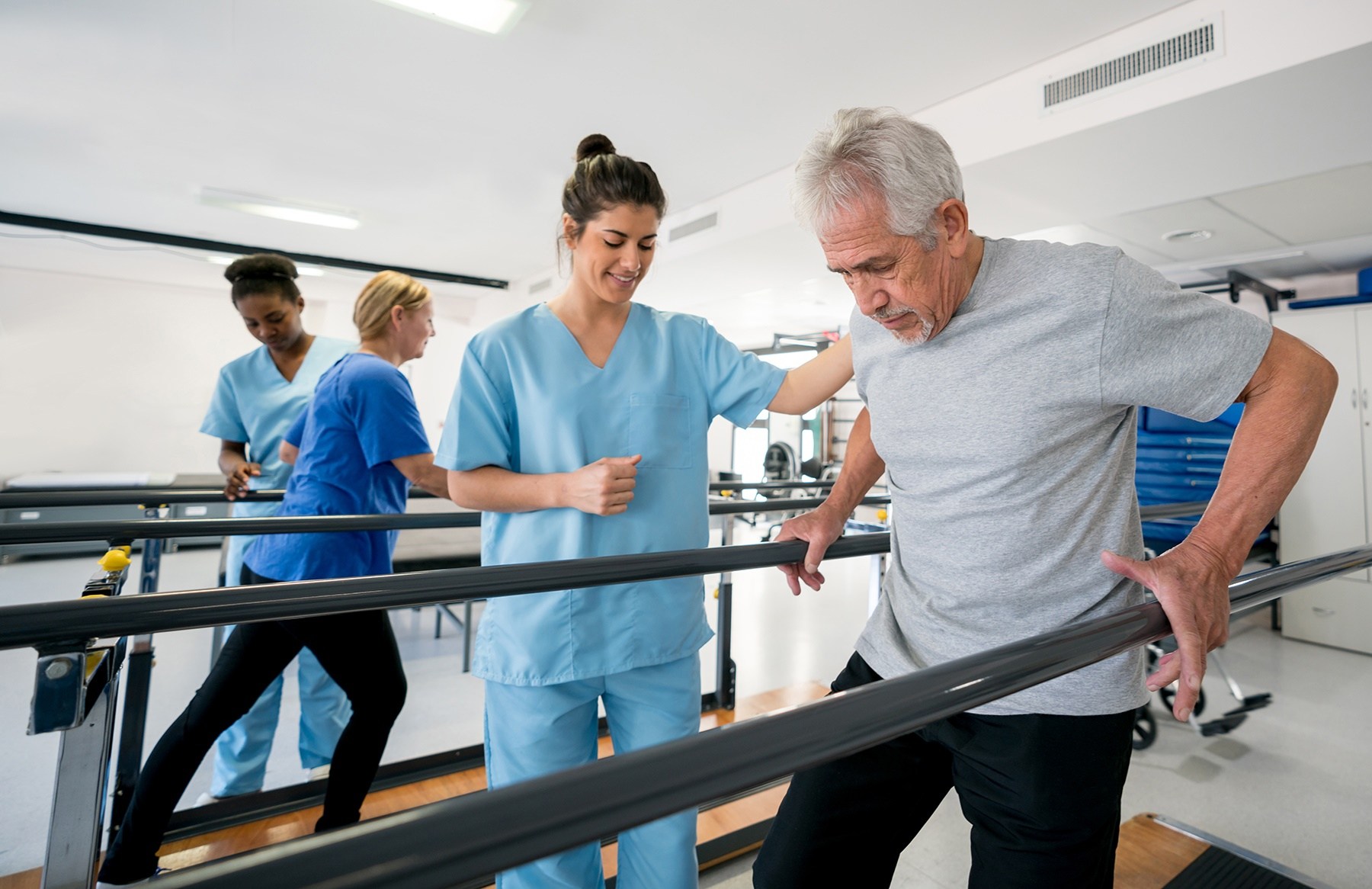 Diverse team of physiotherapist helping patients walk between parallel bars